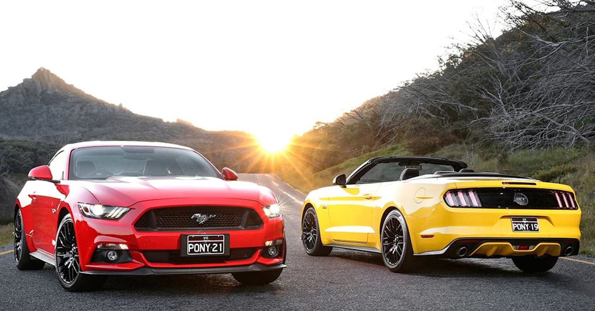 Red Mustang next to Yellow Mustang on road at sunset