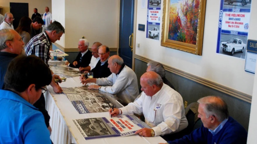 Some original Shelby American team members signing memorabilia at a Shelby American Automobile Club event